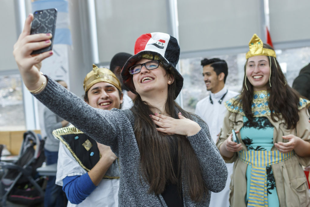 Group of students dressed in cultural costumes smiling and taking a selfie at an international festival event